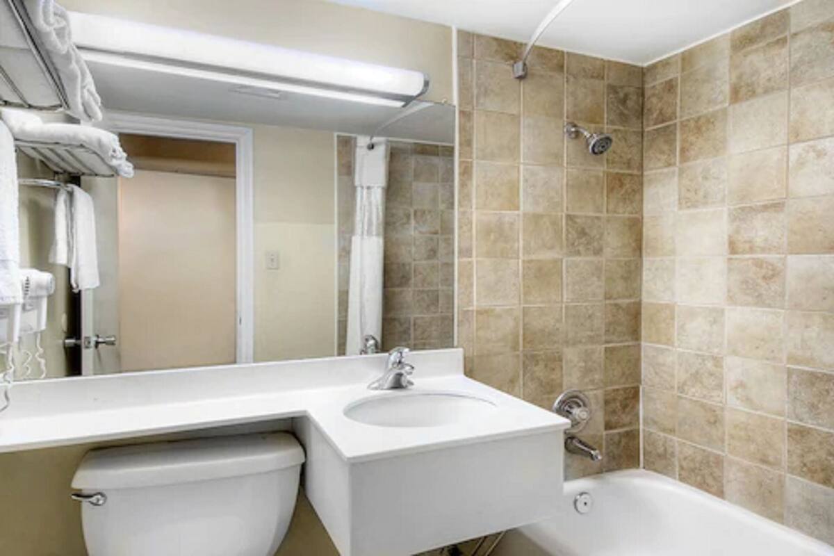 Baño con lavamanos blanco, espejo, ducha y paredes con baldosas color beige.