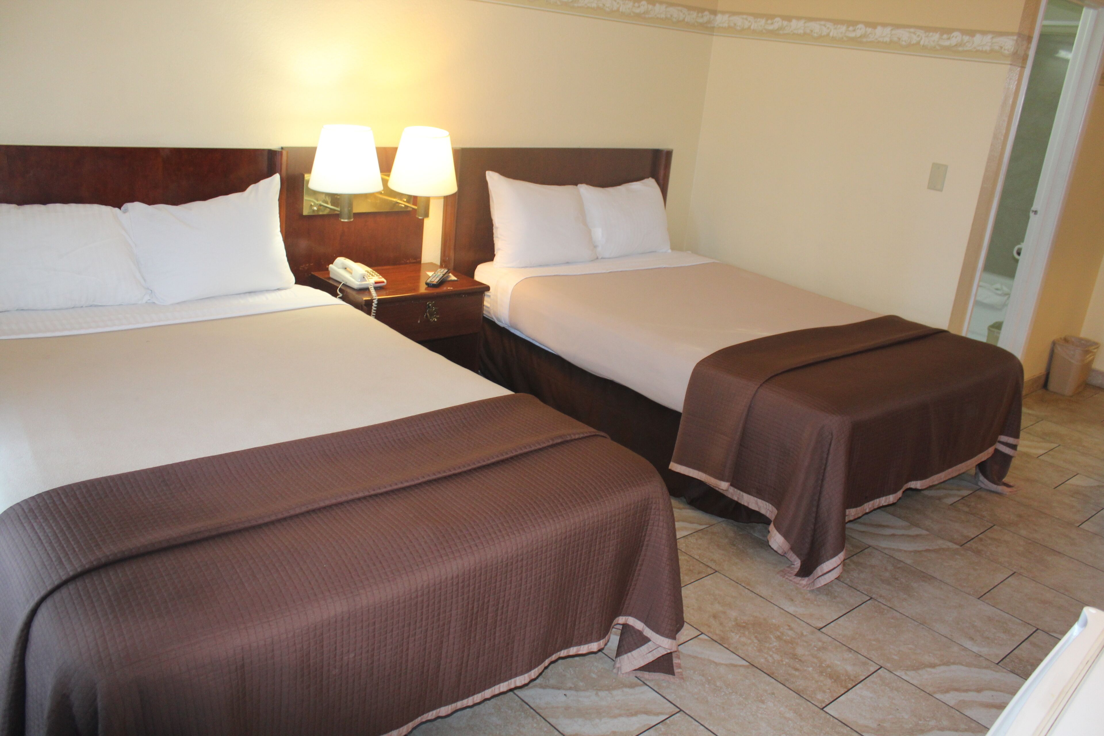 Two adjacent beds with brown bedspreads, a nightstand with a lamp, and a telephone.
