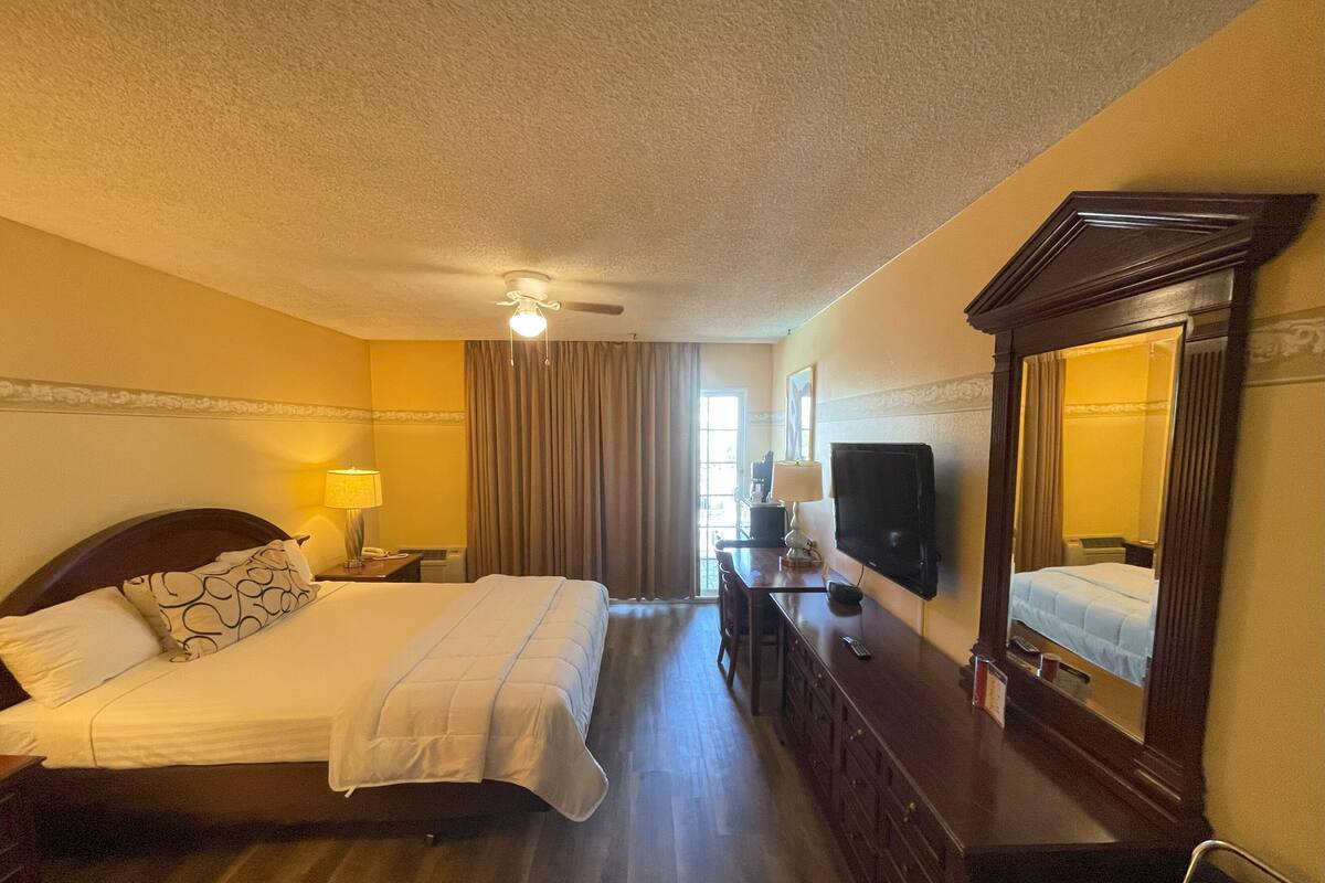 Habitación de hotel con cama, escritorio, silla, televisor, espejo y ventilador de techo.