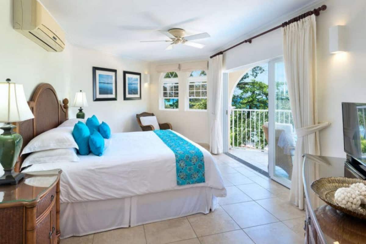 A hotel room with a large bed, a ceiling fan, a balcony with curtains, and a television.