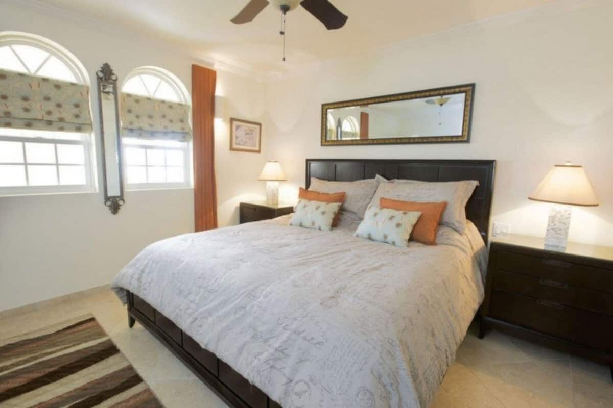 A bedroom with a large bed, two bedside tables with lamps, a ceiling fan, and a large mirror on the wall.