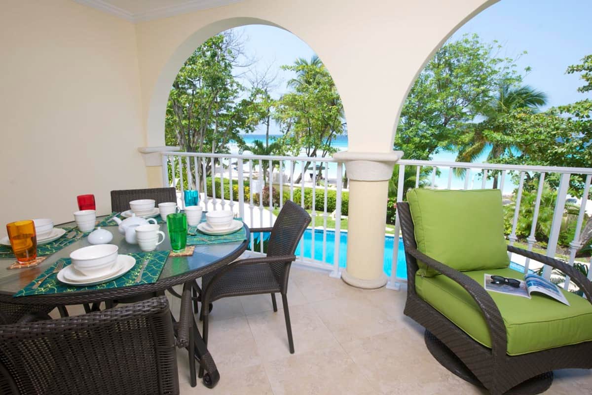 A balcony with a dining table set for two, chairs, and a view of the ocean.