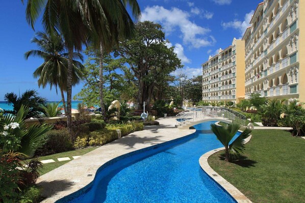 A resort with a swimming pool, palm trees, and a building with balconies. - Sapphire Beach Condominiums by Blue Sky Luxury (St. Lawrence Gap)