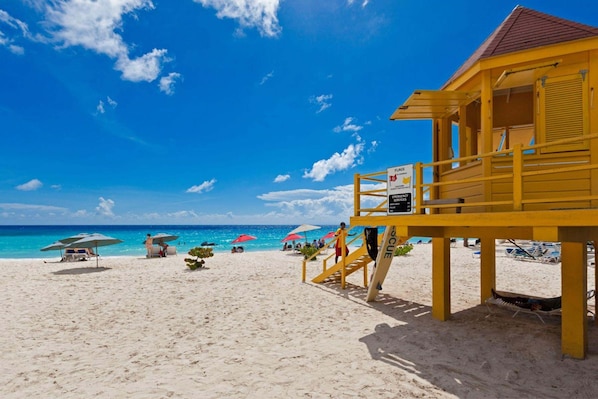 A beach with a lifeguard tower, umbrellas, and beach chairs. - Sapphire Beach Condominiums by Blue Sky Luxury (St. Lawrence Gap)