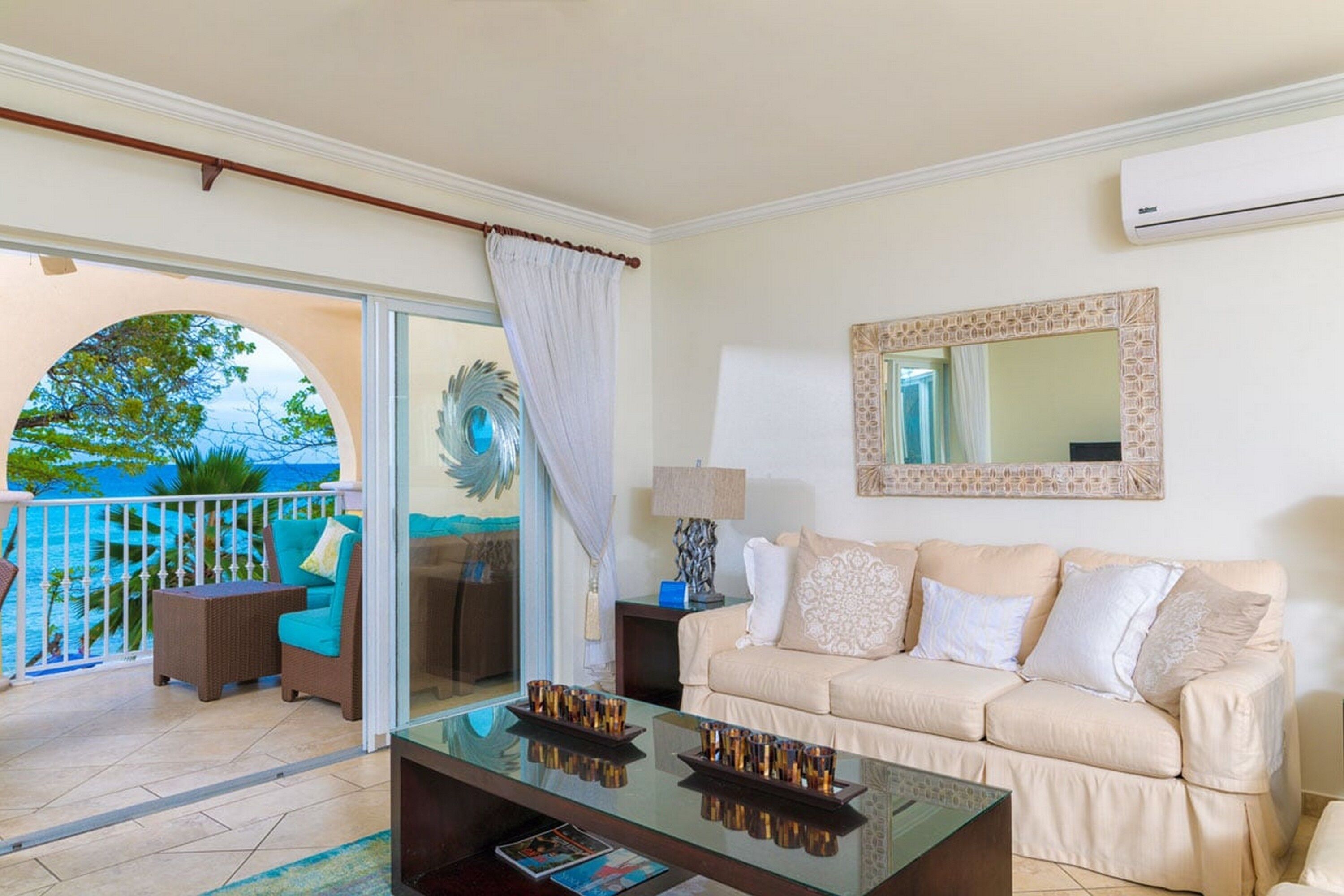 A living room with a sofa, a coffee table, and a view of the ocean through a glass door.