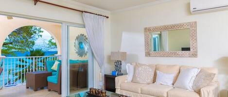A living room with a sofa, a coffee table, and a view of the ocean through a glass door.