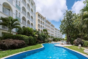 Un hotel con piscina, palmeras y un edificio de varios pisos con balcones.