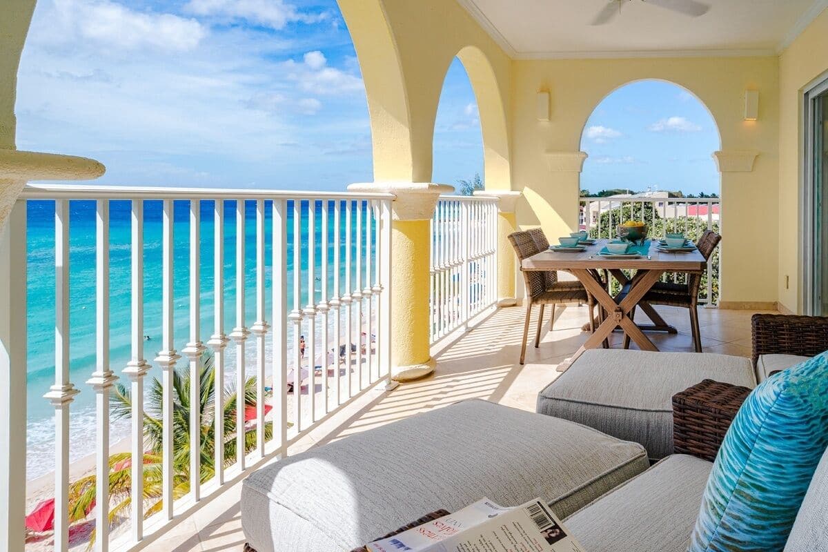 A balcony with a view of the ocean, a dining table with chairs, and a sofa with cushions.