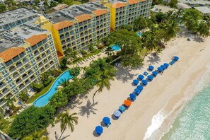 A resort with a pool, beach umbrellas, and a building with multiple balconies. - Sapphire Beach Condominiums by Blue Sky Luxury (St. Lawrence Gap)