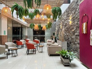 A modern indoor space with seating areas, hanging plants, and a stone wall. - Hotel El Tambo 2 (Lima)