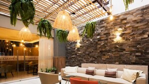 Un espacio lounge moderno con pared de piedra, un sofá, dos sillones y plantas colgantes.