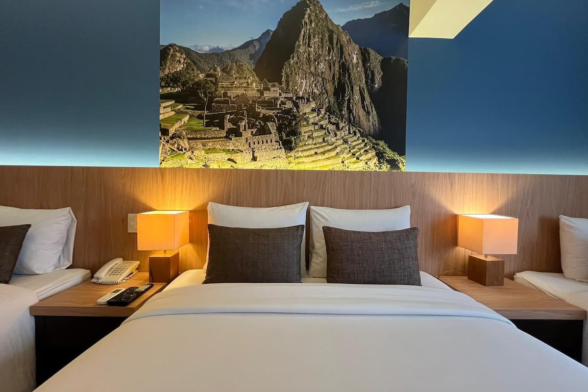 Camera d'albergo con un letto grande, due comodini, un telefono e un quadro appeso al muro con vista su Machu Picchu.