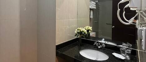 Un baño moderno con lavamanos de mármol negro, un espejo grande, un secador de pelo de mano y un perchero para toallas.