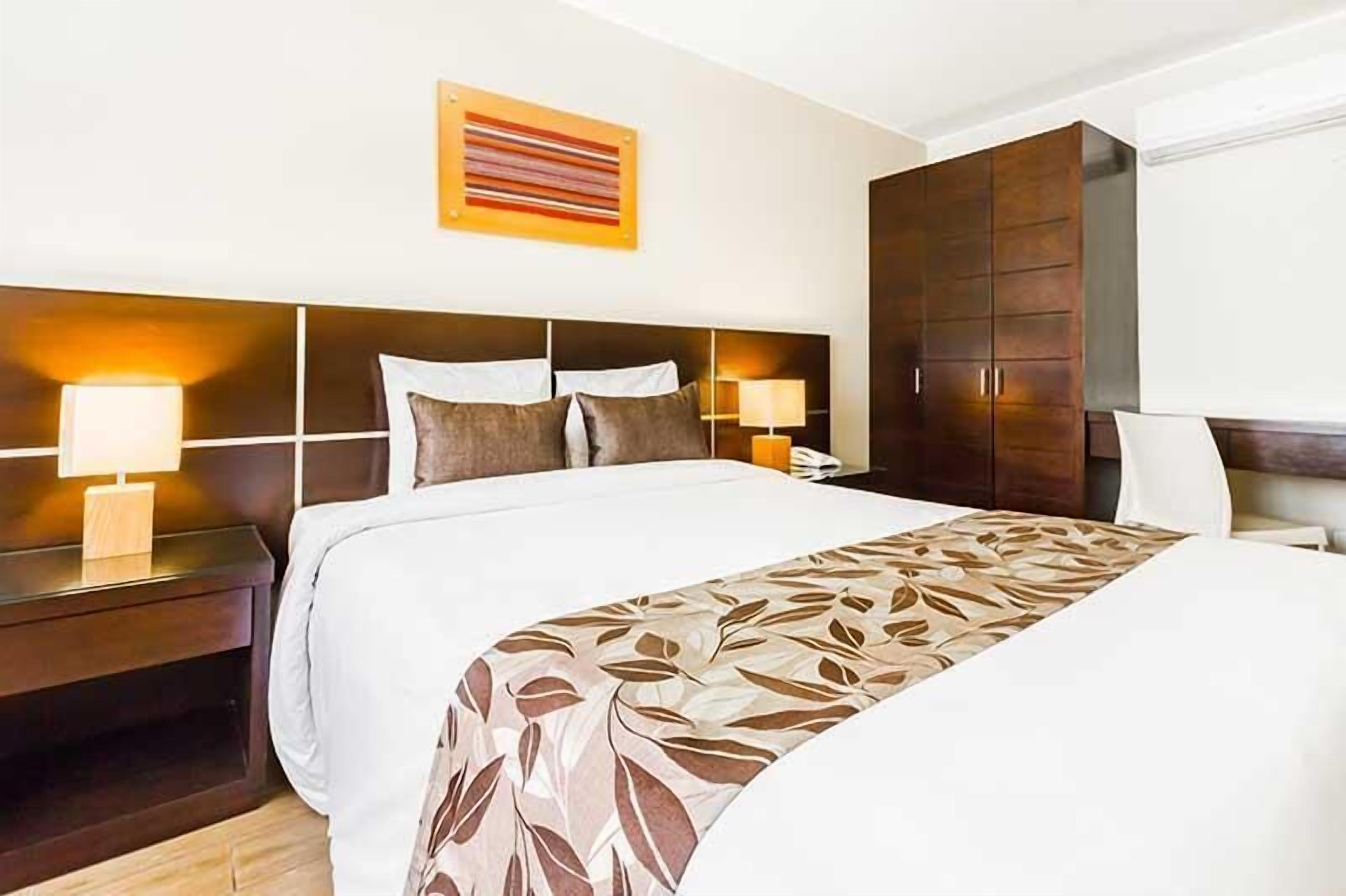 Une chambre d’hôtel avec un grand lit, deux tables de chevet avec des lampes, une armoire et une œuvre d’art accrochée au mur.