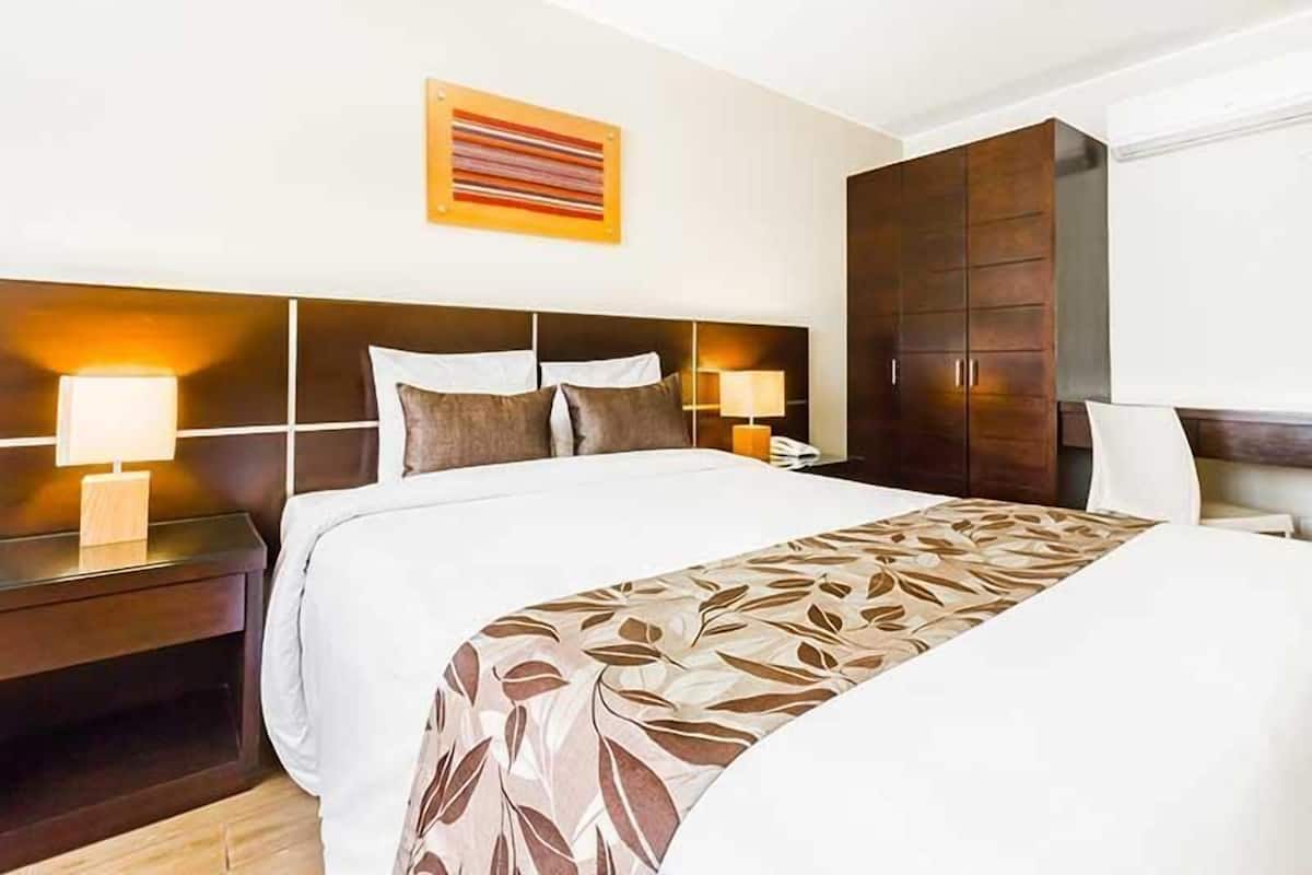 Habitación de hotel con una cama grande, dos mesitas de noche con lámparas, un armario y una obra de arte colgada en la pared.