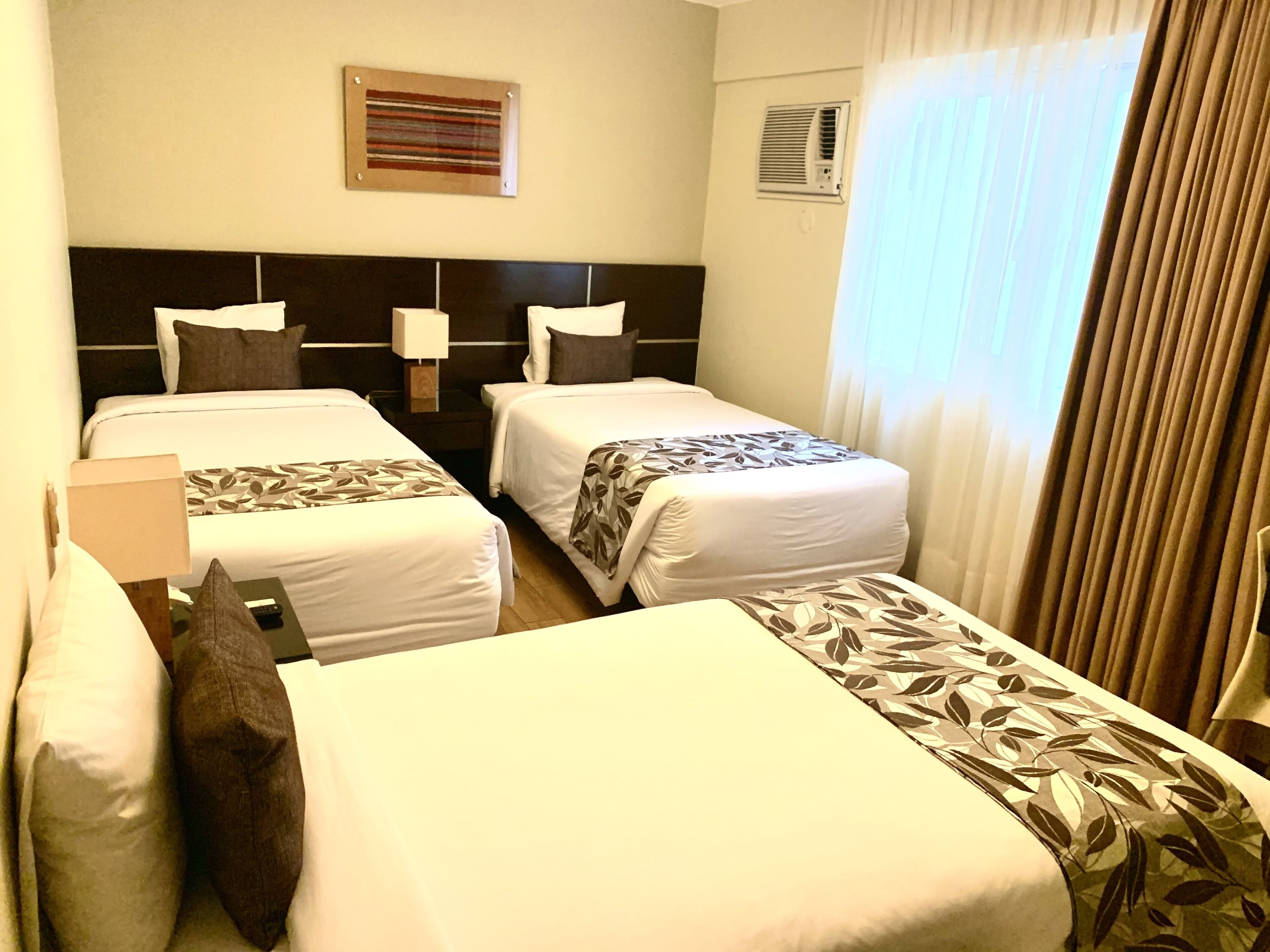 Une chambre d’hôtel avec deux lits simples, une tête de lit, des tables de chevet, une lampe et une fenêtre avec des rideaux.