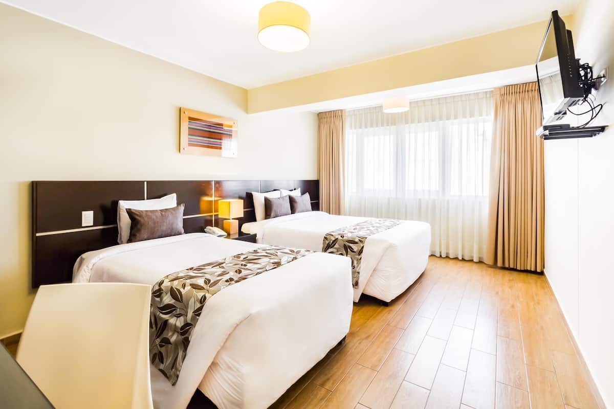 Camera d'albergo con due letti, una scrivania, una sedia, una televisione e una finestra con tende.