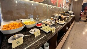 Un bufé con cuencos etiquetados de papaya y piña, una variedad de quesos y una estación de café.