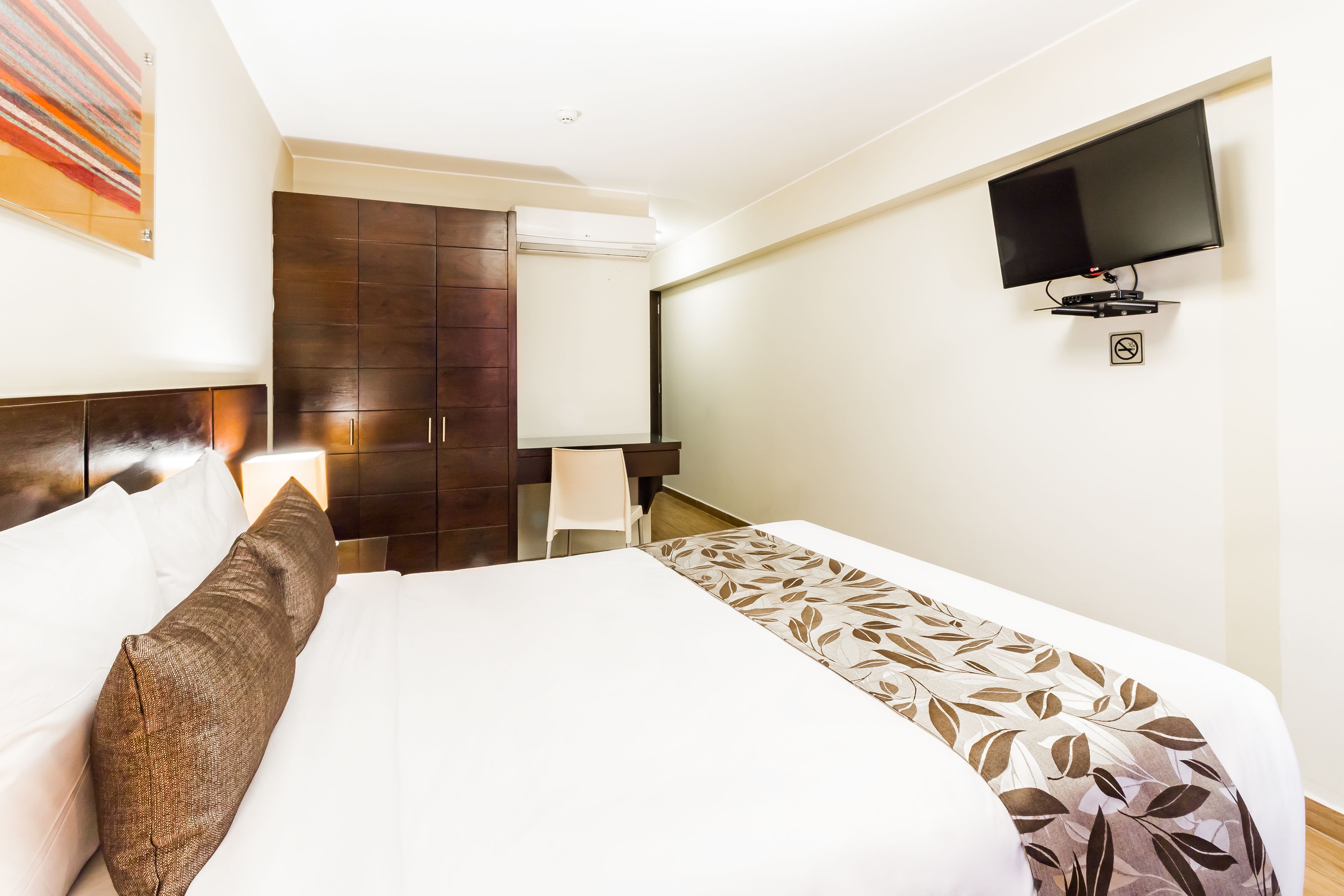 Habitación de hotel con una cama grande, un televisor de pantalla plana montado en la pared, un armario y un escritorio con una silla.