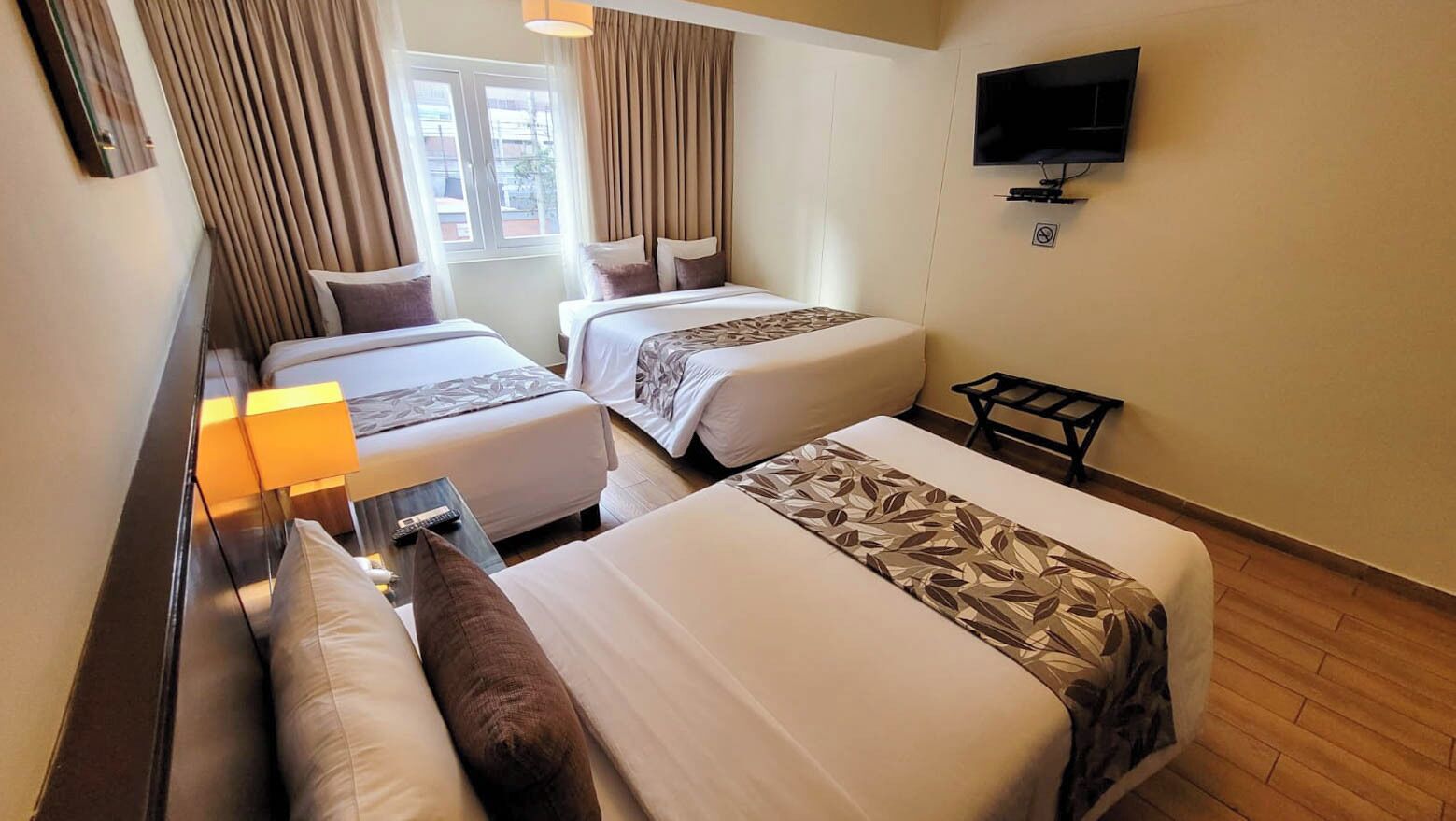 A hotel room with two beds, a TV, and a window with curtains.