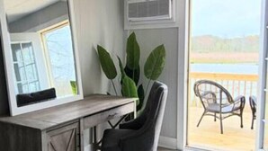 Una habitación con un escritorio de madera, una silla, un espejo grande y vistas al exterior a través de una puerta corredera.