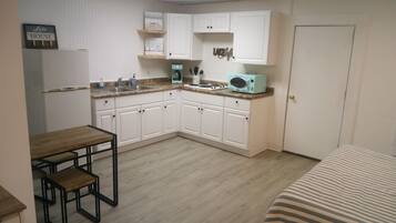 A compact kitchen with white cabinets, a refrigerator, a microwave, and a coffee maker on the countertop.