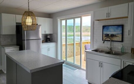 A modern kitchen with white cabinets, a stainless steel refrigerator, a hanging light fixture, and a large sliding glass door leading to an outdoor deck.