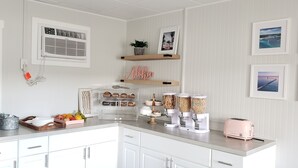 Una cocina moderna con armarios blancos, una encimera con alimentos, un tostador y estantes decorativos.