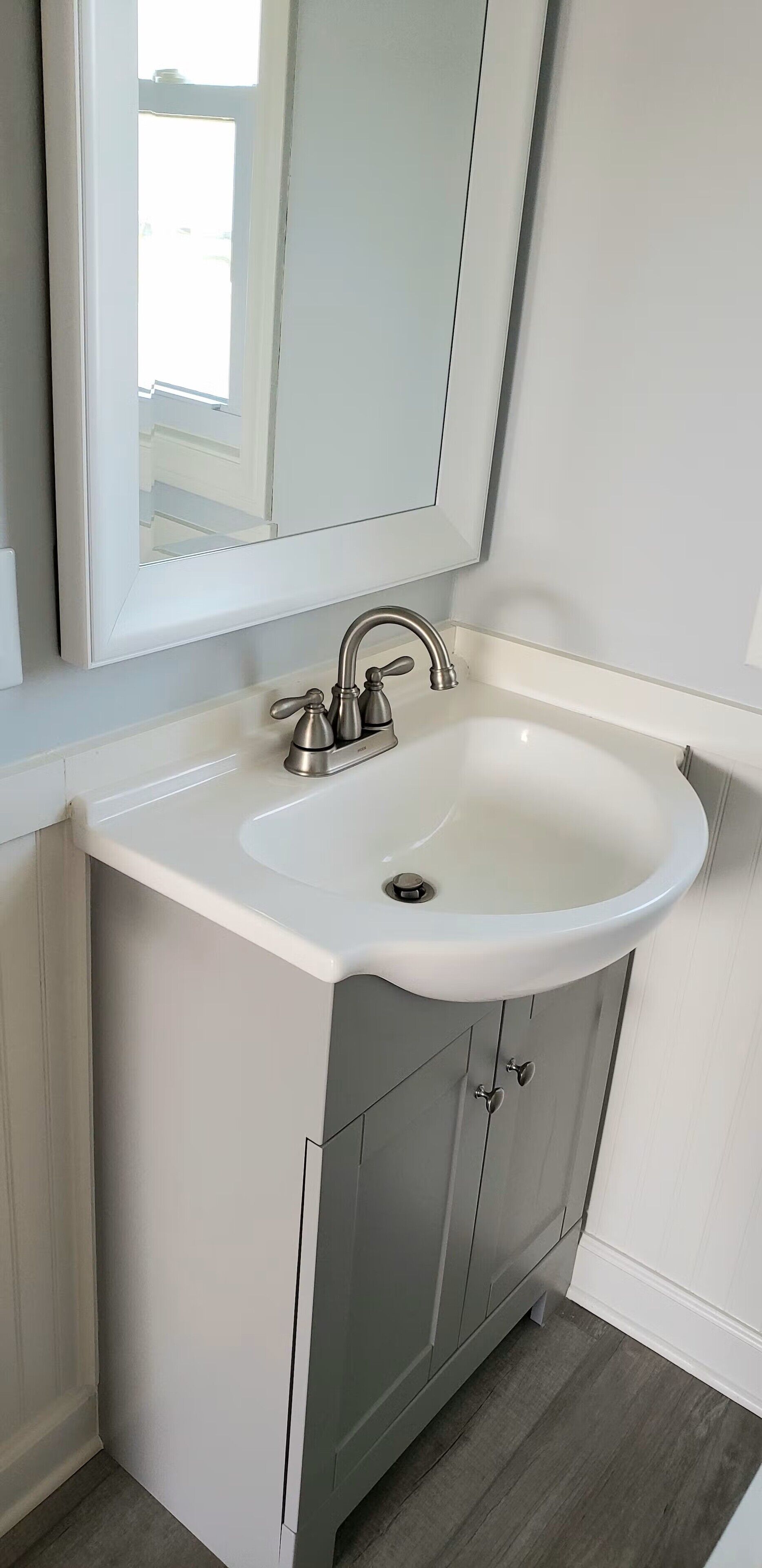 A bathroom with a white sink, a mirror, and a cabinet with a heart-shaped handle.