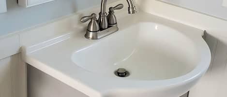A bathroom with a white sink, a mirror, and a cabinet with a heart-shaped handle.