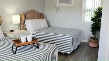 Quarto de hotel com duas camas, uma mesa de cabeceira com abajur, um relógio digital e uma bandeja com duas canecas.