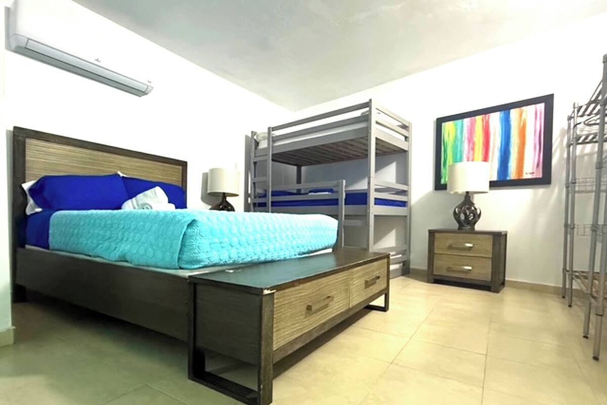 Une chambre à coucher comprenant un lit, un bureau, une chaise, une armoire, une lampe et un tableau coloré accroché au mur.