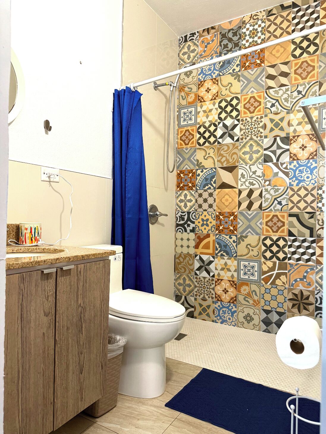 Un baño con inodoro, ducha con cortina azul y pared de azulejos con diversos diseños.