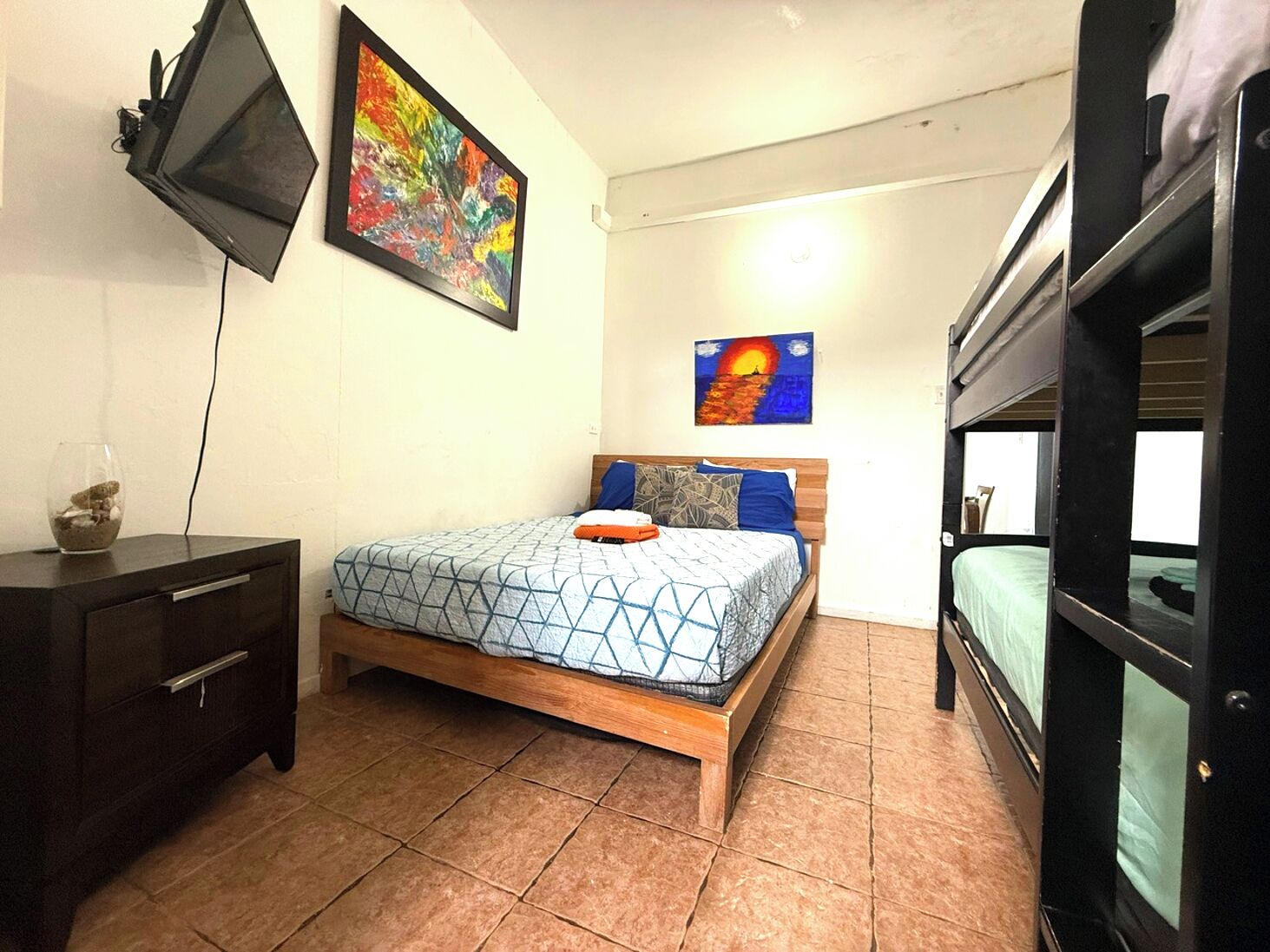 A bedroom with a bed, a TV, and artwork on the walls.