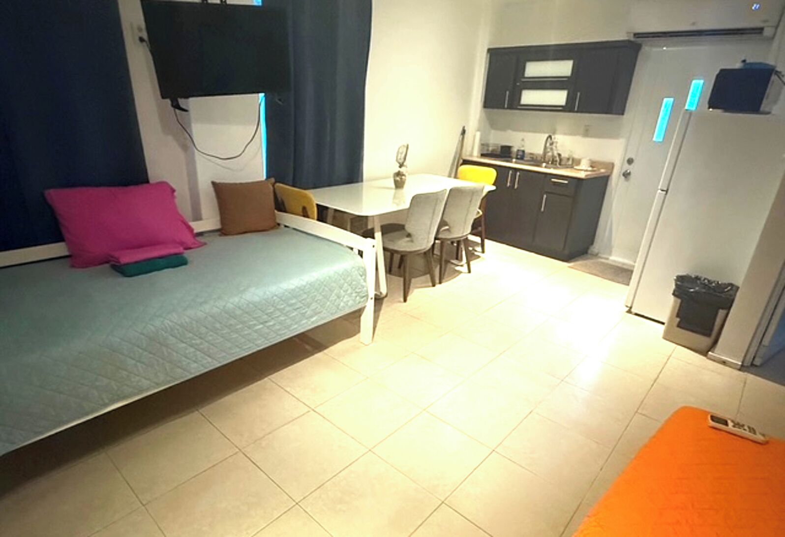 A compact room with a bed, a small dining table, and a kitchenette.