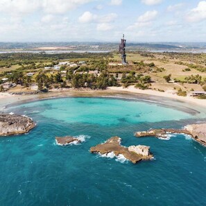 A coastal area with a clear turquoise sea, rocky outcrops, and a distant tower. - Ventana al Atlantico at Arecibo 681 Ocean Drive (Arecibo)