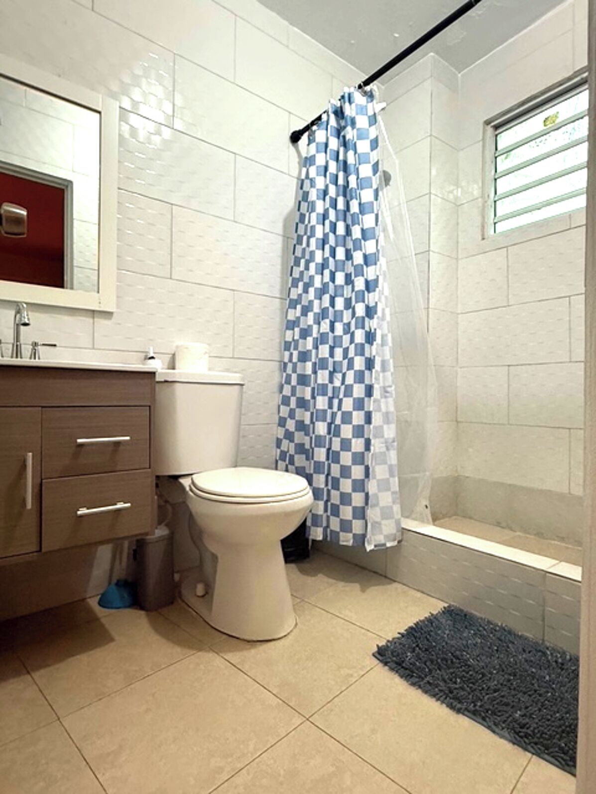 Een badkamer met toilet, wastafel met spiegel, douchegordijn blauw-wit geruit en een raam met zonwering.