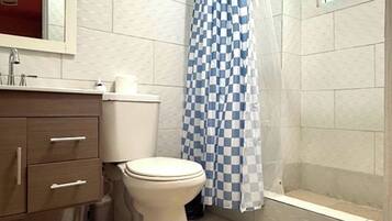 Een badkamer met toilet, wastafel met spiegel, douchegordijn blauw-wit geruit en een raam met zonwering.