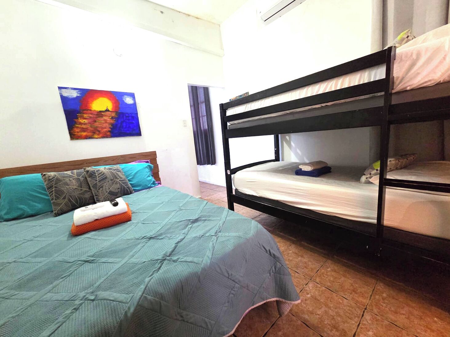 A room with a bed, a bunk bed, a painting, and a window with curtains.