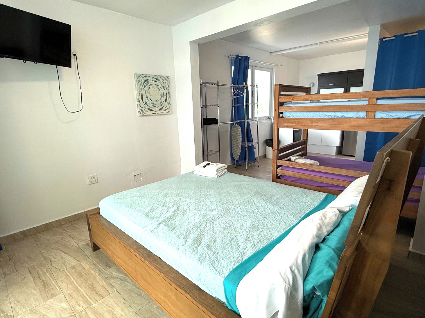 A bedroom with a bunk bed, a flat-screen TV mounted on the wall, a small ironing board, and a window with curtains.