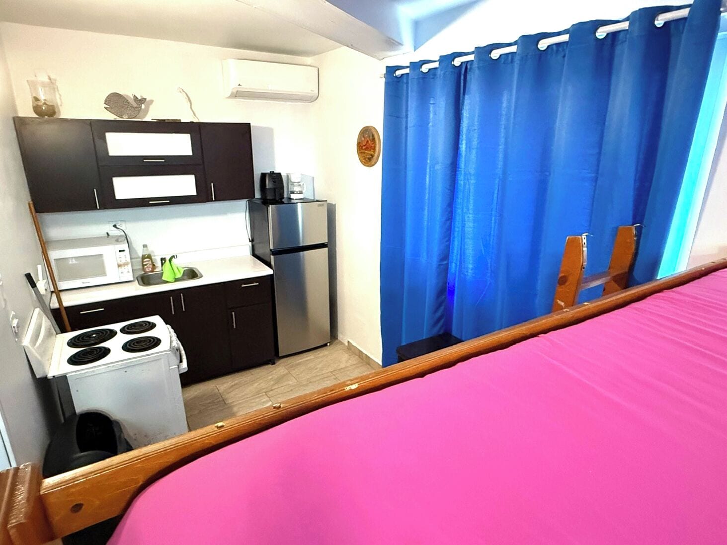A compact kitchenette with a microwave, stove, and refrigerator, a small sink, and a blue curtain.