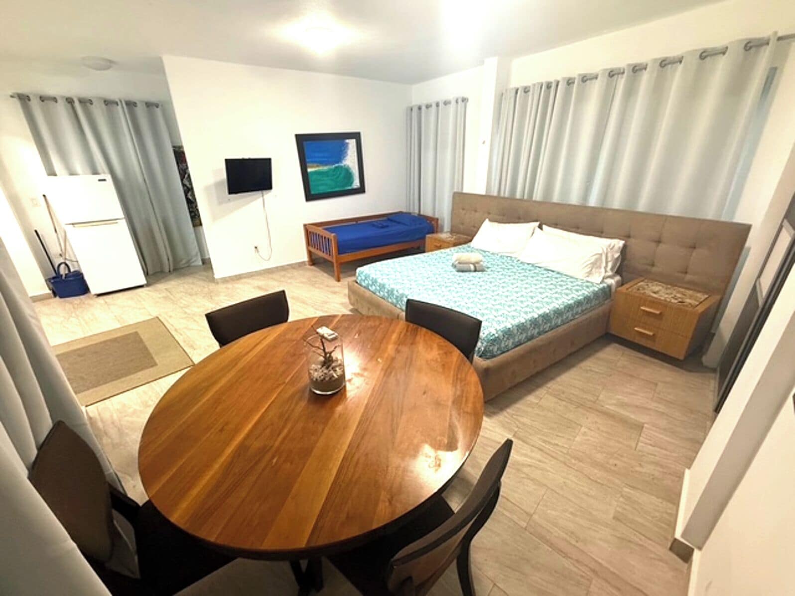 A bedroom with a bed, a TV, a desk, and a dining table.