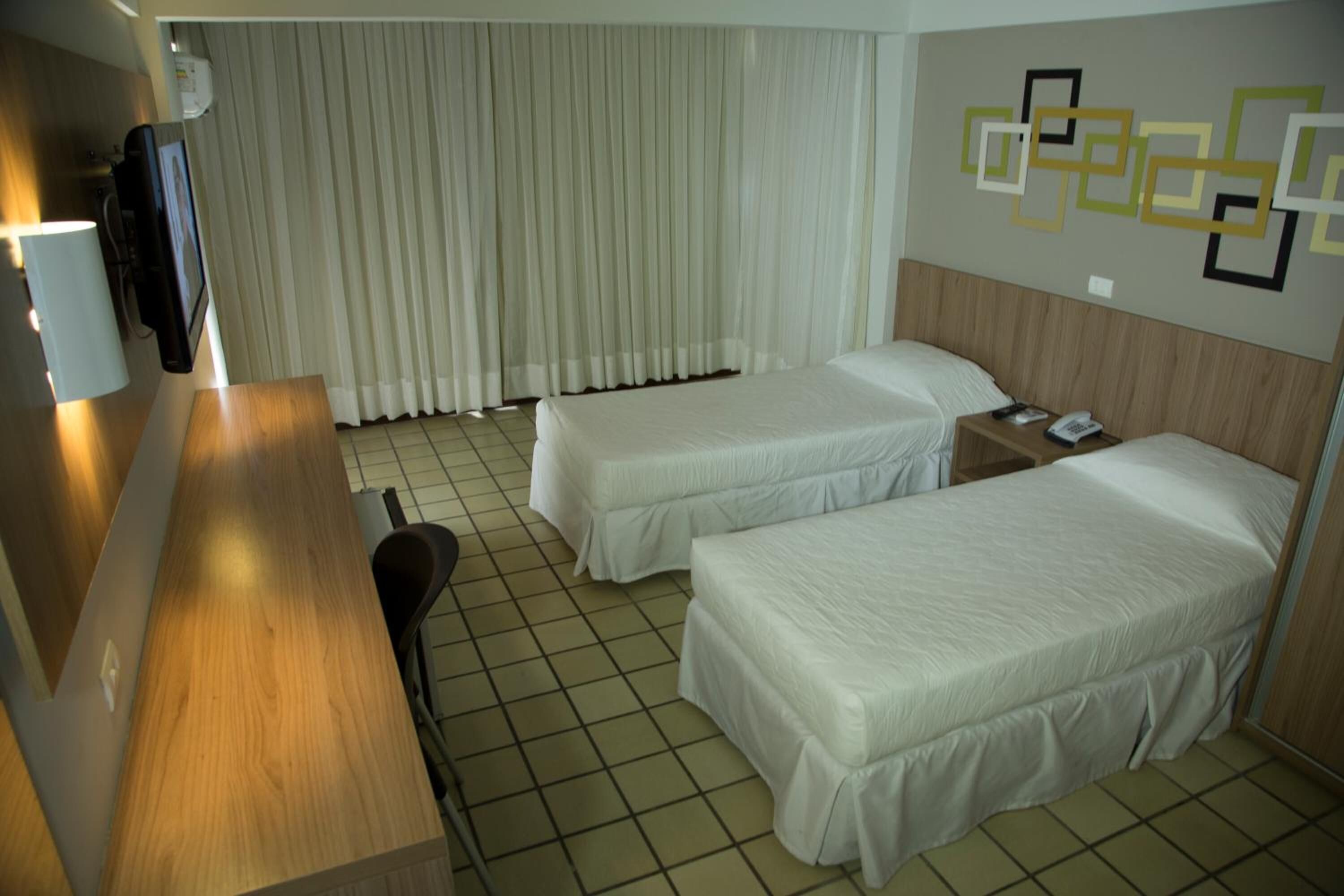 A hotel room with two beds, a desk, a chair, and a TV.
