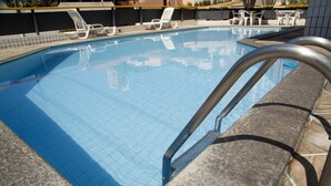 Una piscina con agua cristalina azul, rodeada de sillas de descanso y un deck de azulejos.