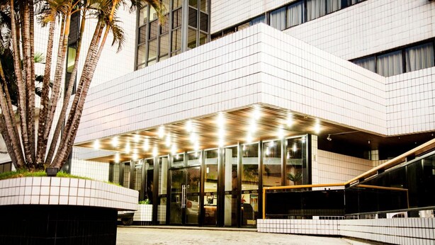 Un edificio moderno con fachada de tejas, un amplio acceso de vidrio y un área exterior cubierta con palmeras.