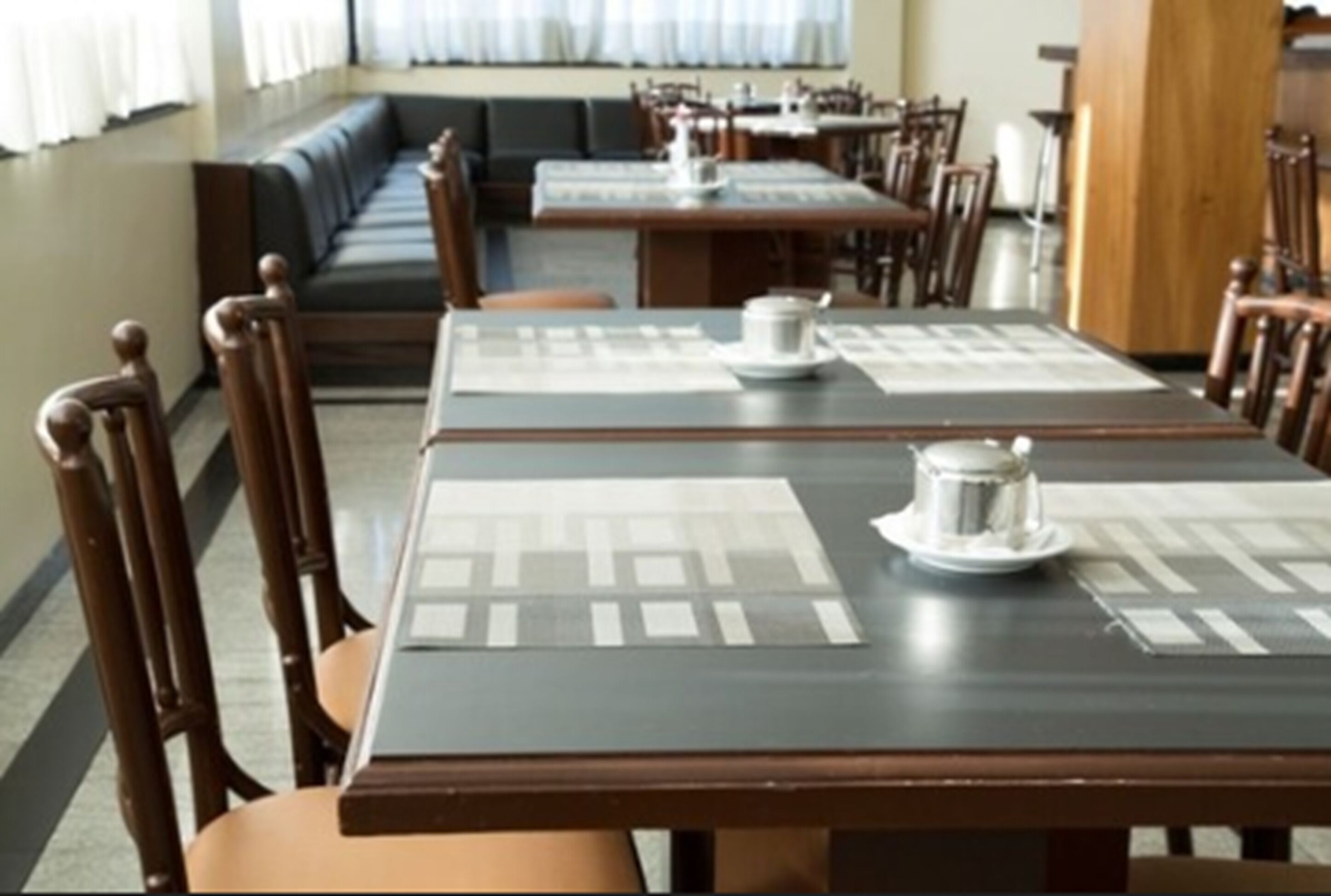 Un restaurante con mesas y sillas de madera, una zona de estar con un largo banco y una barra.