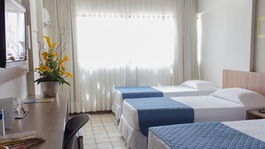 Habitación de hotel con dos camas, un escritorio, una silla, una planta en maceta y una ventana con cortinas.