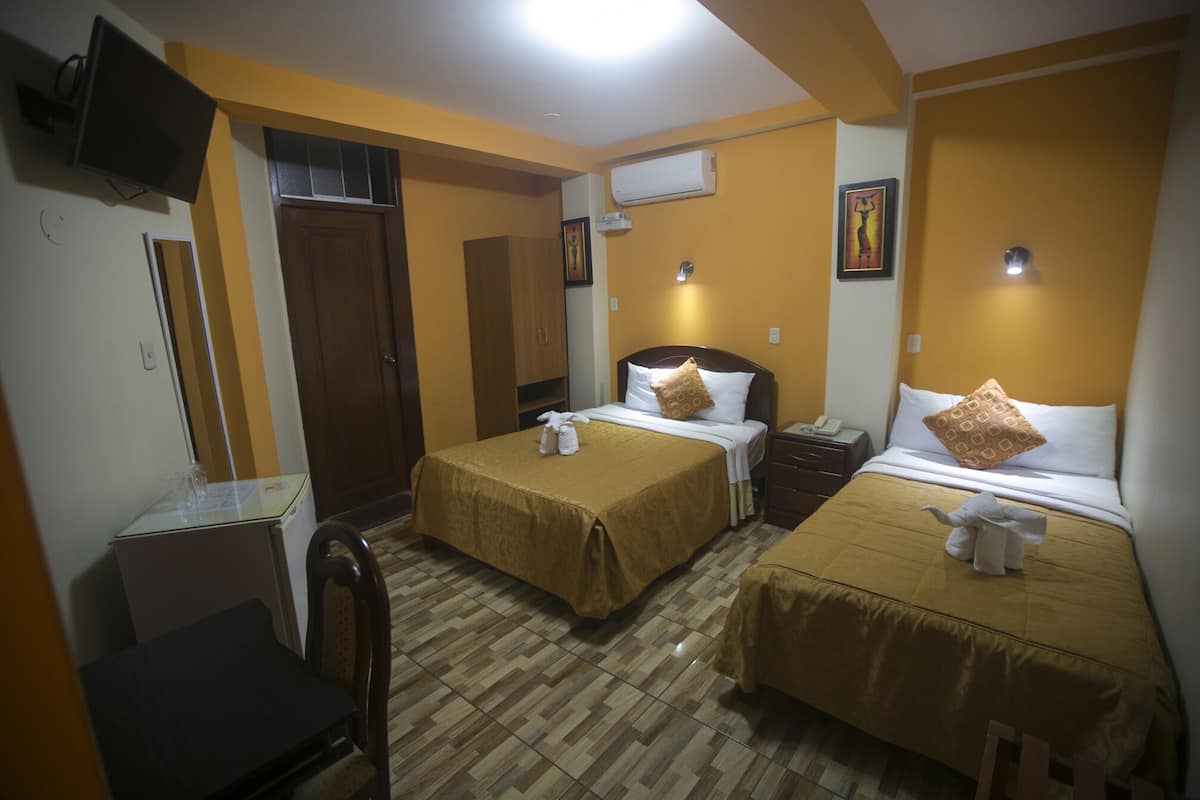 Quarto de hotel com duas camas, uma escrivaninha, uma cadeira e uma televisão.