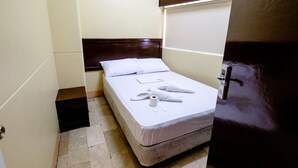 Een klein, net opgemaakt bed met een witte matras en een houten hoofdbord in een compacte kamer met een betegelde vloer.