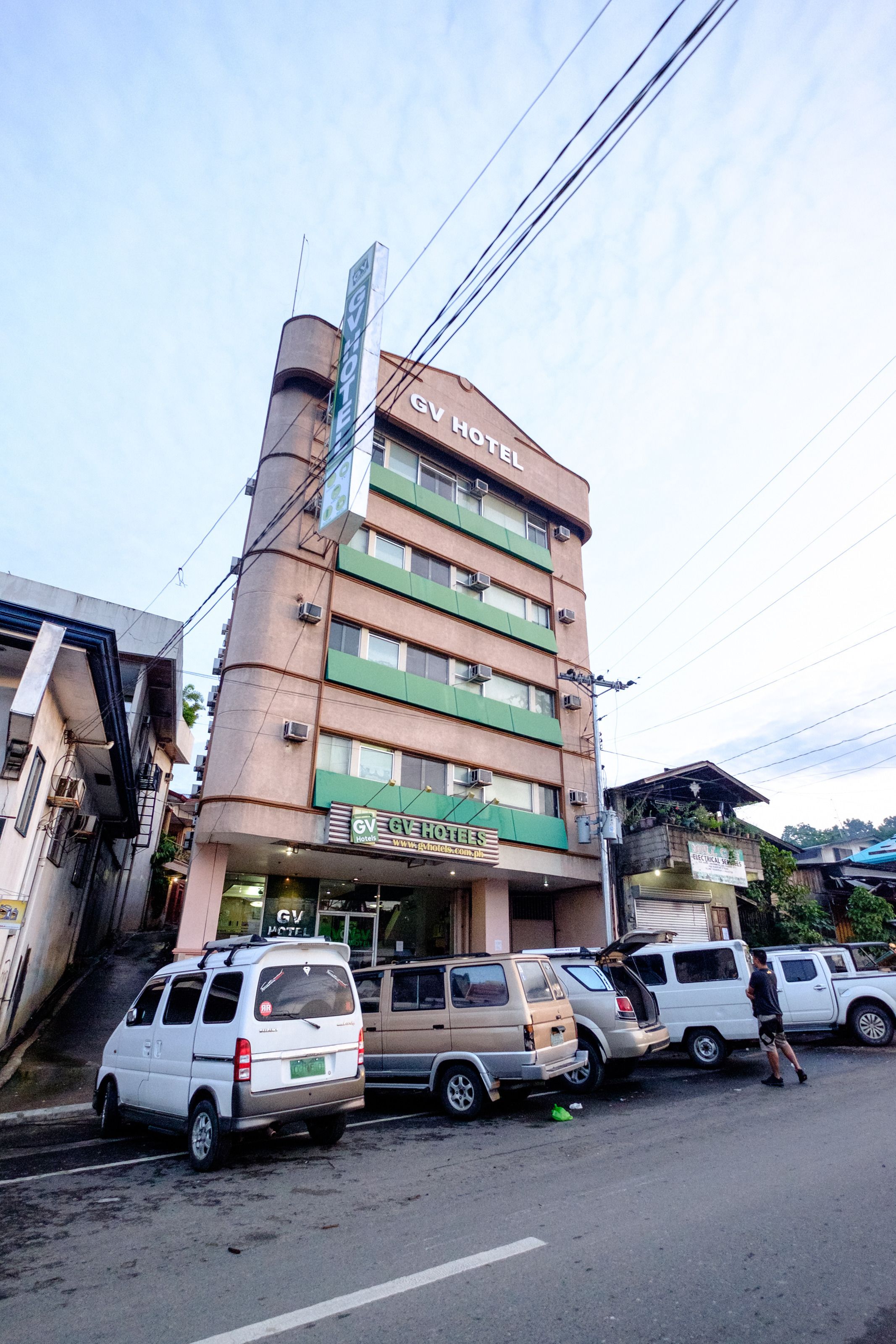 A hotel with multiple floors, a signboard, and several parked vehicles in front.
